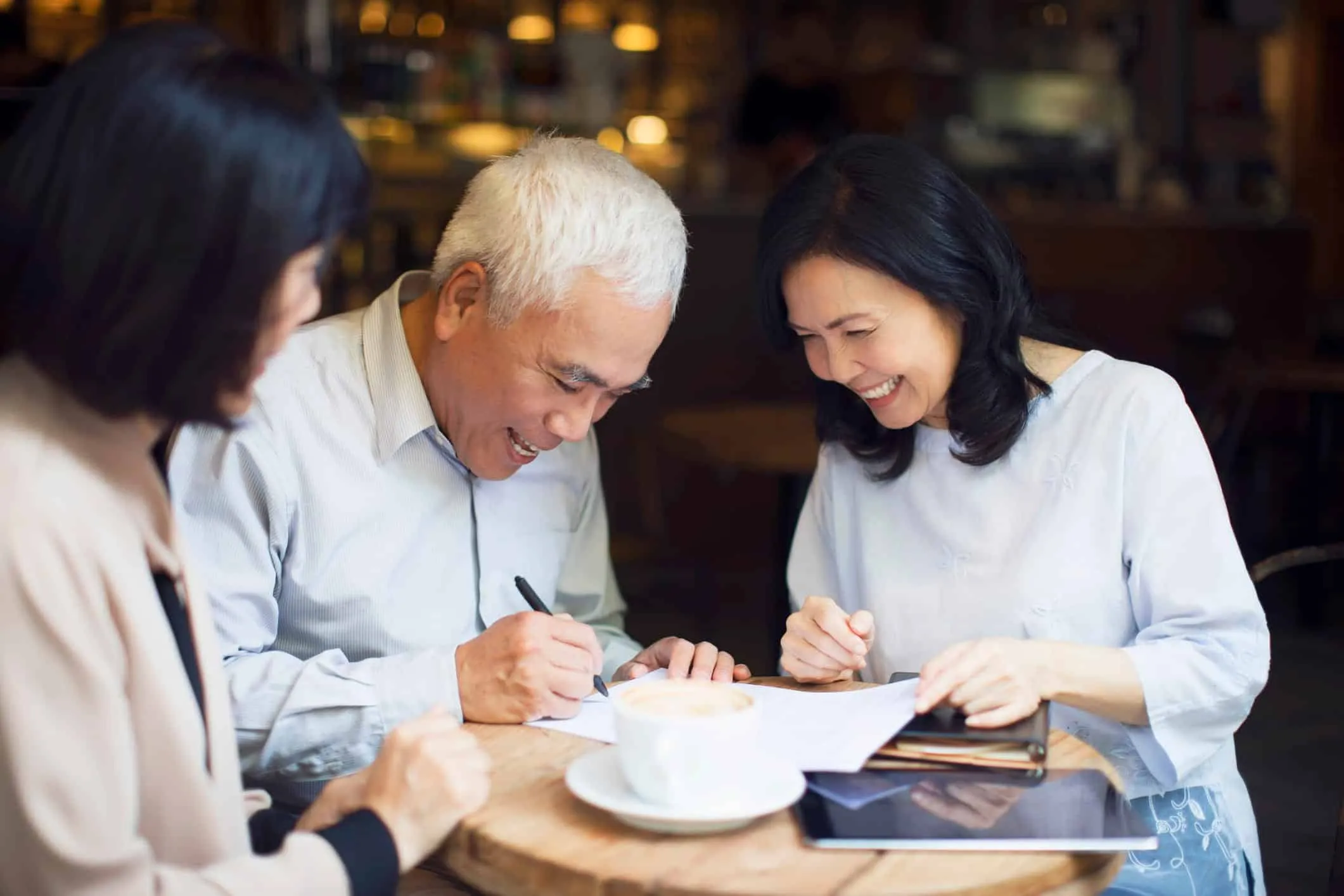 Older man and two women reviewing and signing papers together at a table