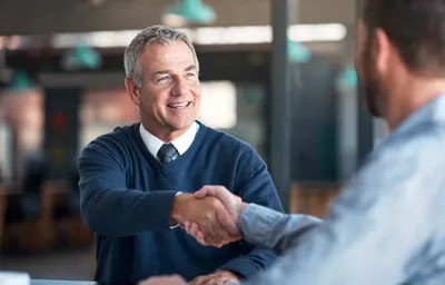 Smiling older businessman shaking hands with a colleague in an office