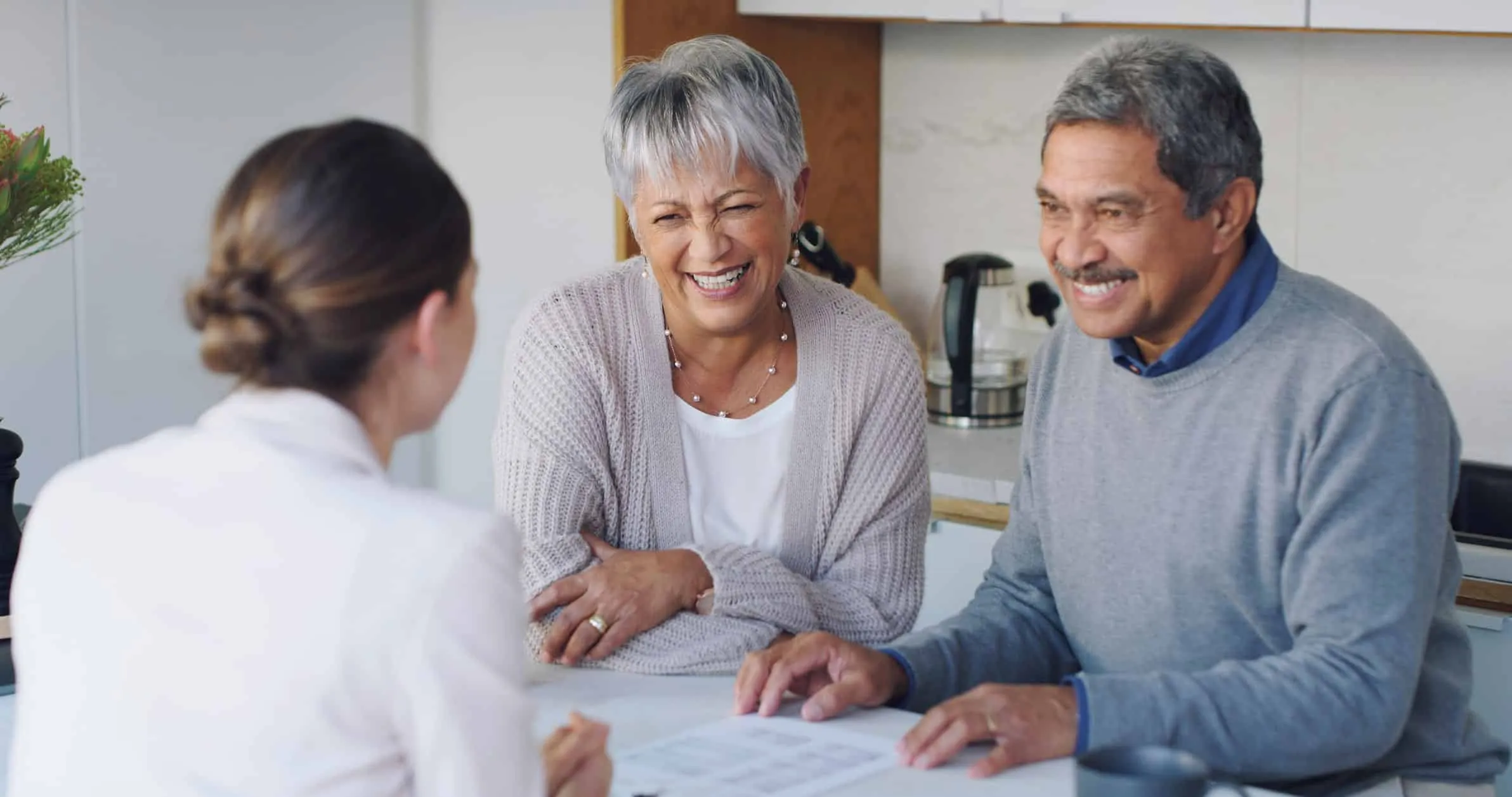 Older couple smiling while reviewing papers with a woman across the table