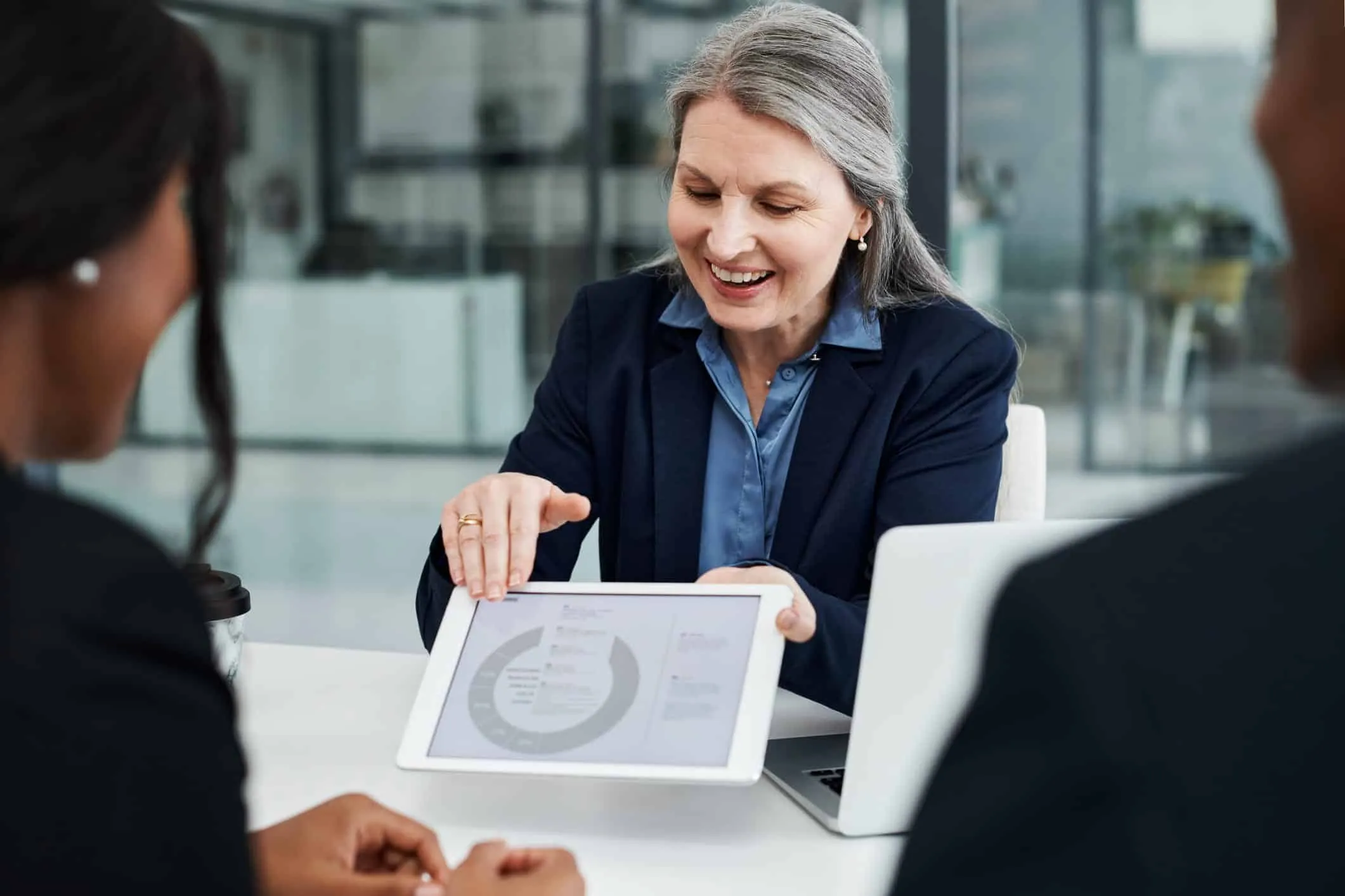 Woman showing a chart on a tablet to two people at a meeting table