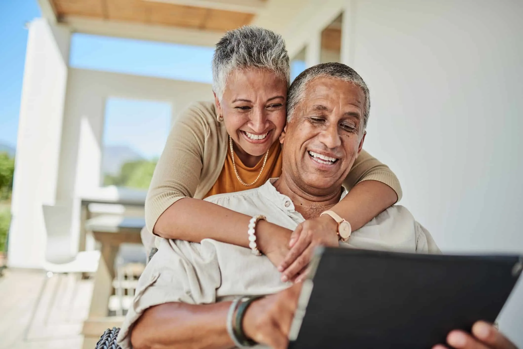Older couple embracing and smiling while looking at a tablet