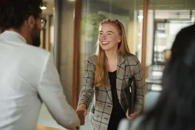 Woman in a plaid blazer smiling and shaking hands with a man