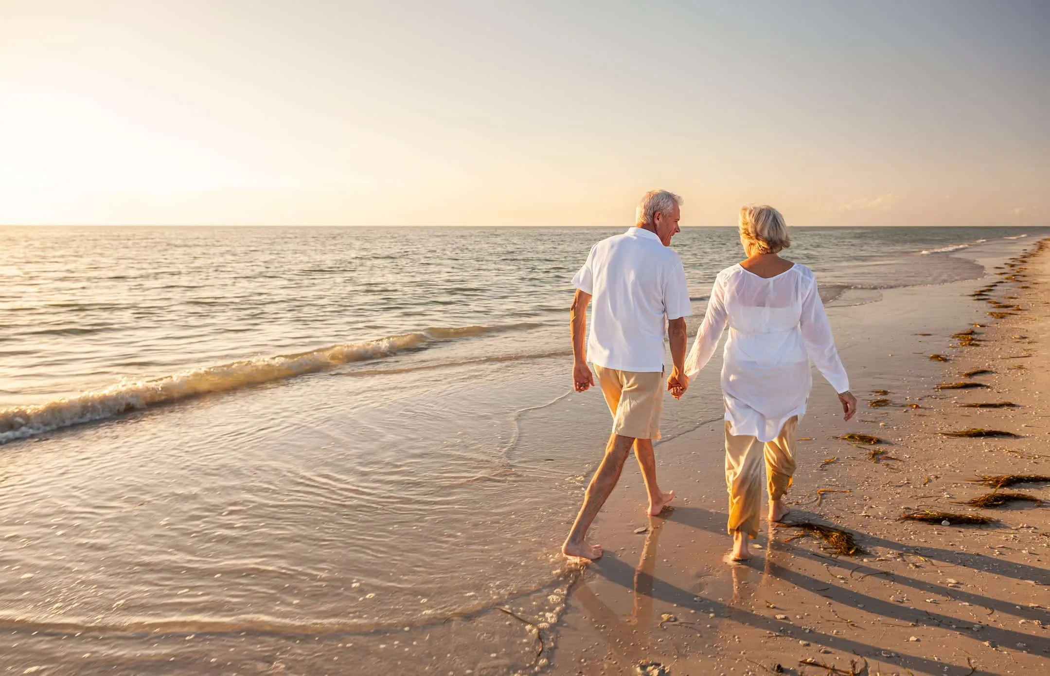 Older couple walking along the shoreline at sunset