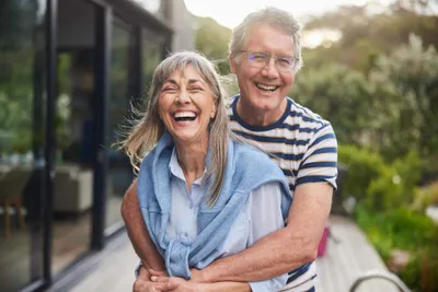 Older couple laughing outdoors, the man hugging the woman from behind