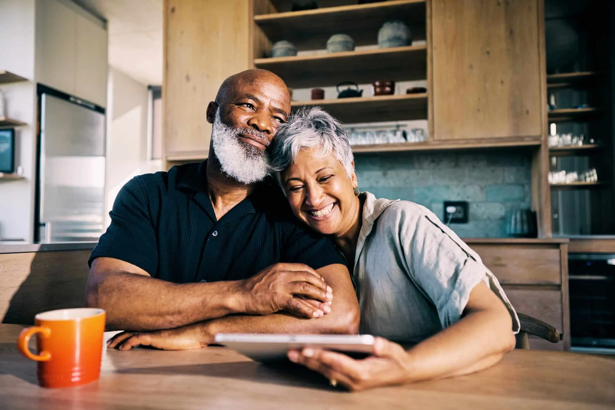 Older couple smiling together at a kitchen table with a tablet