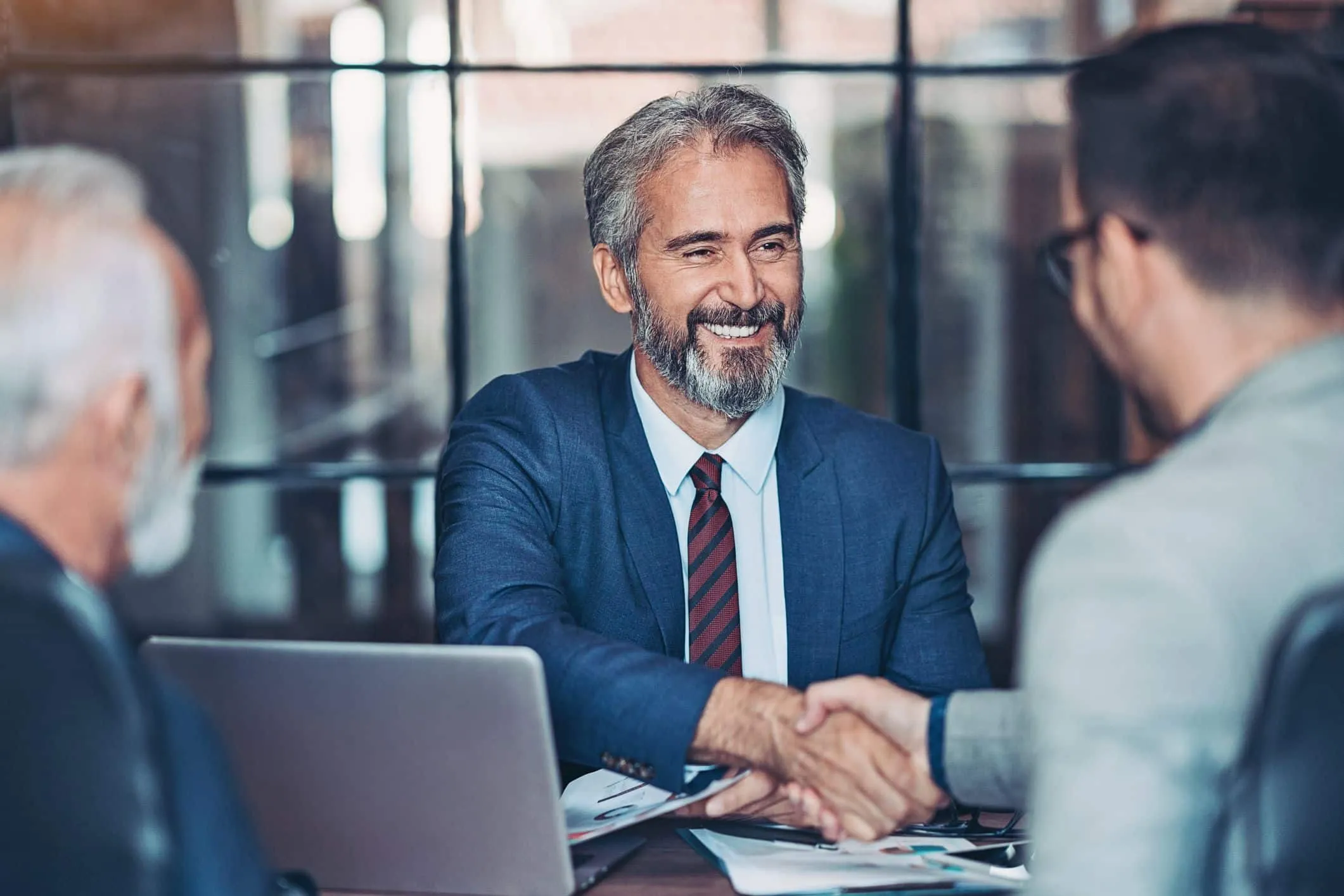 Man in a suit shaking hands with another man across a meeting table