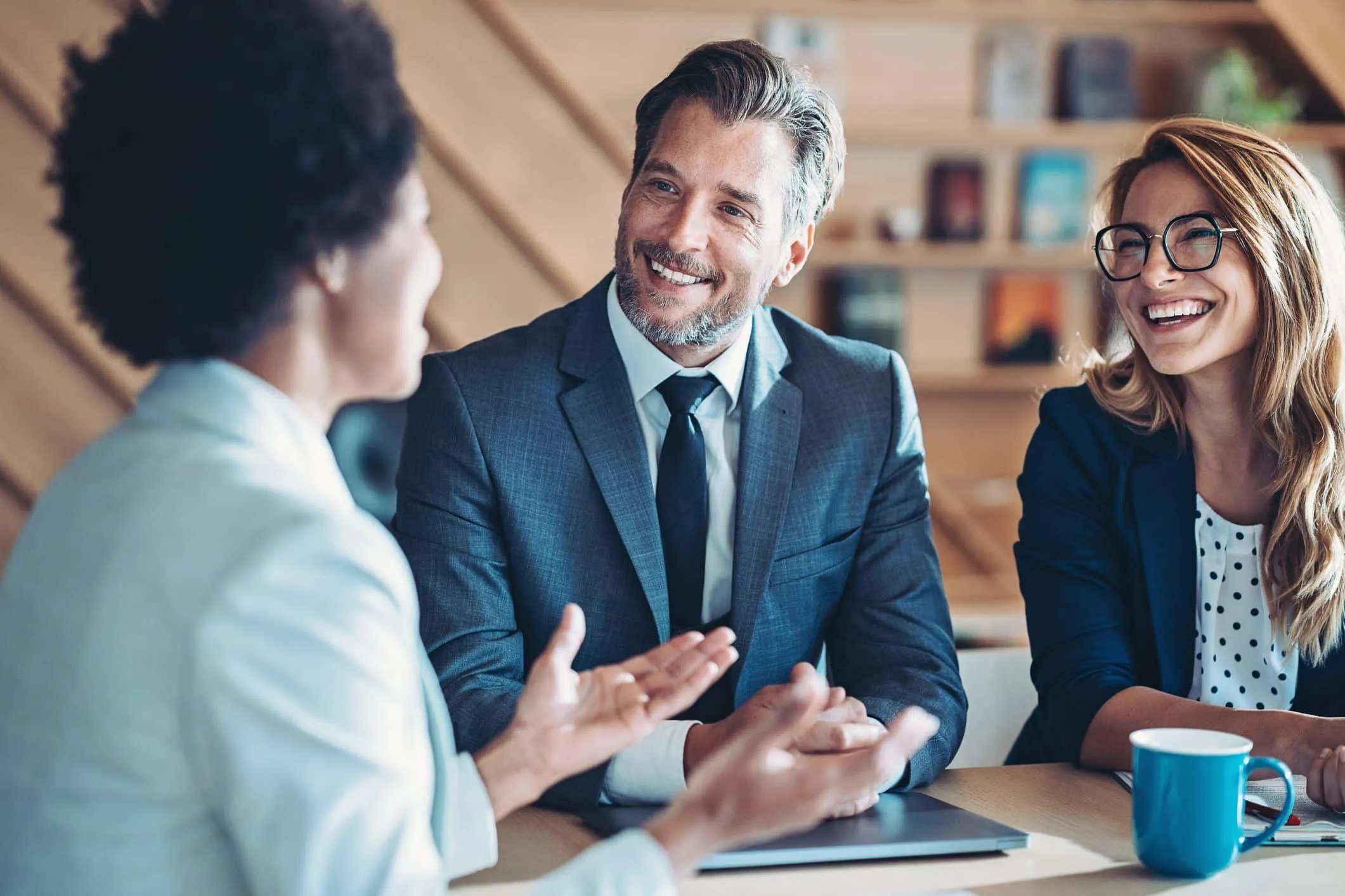 Smiling man in a suit talking with two women at a meeting table