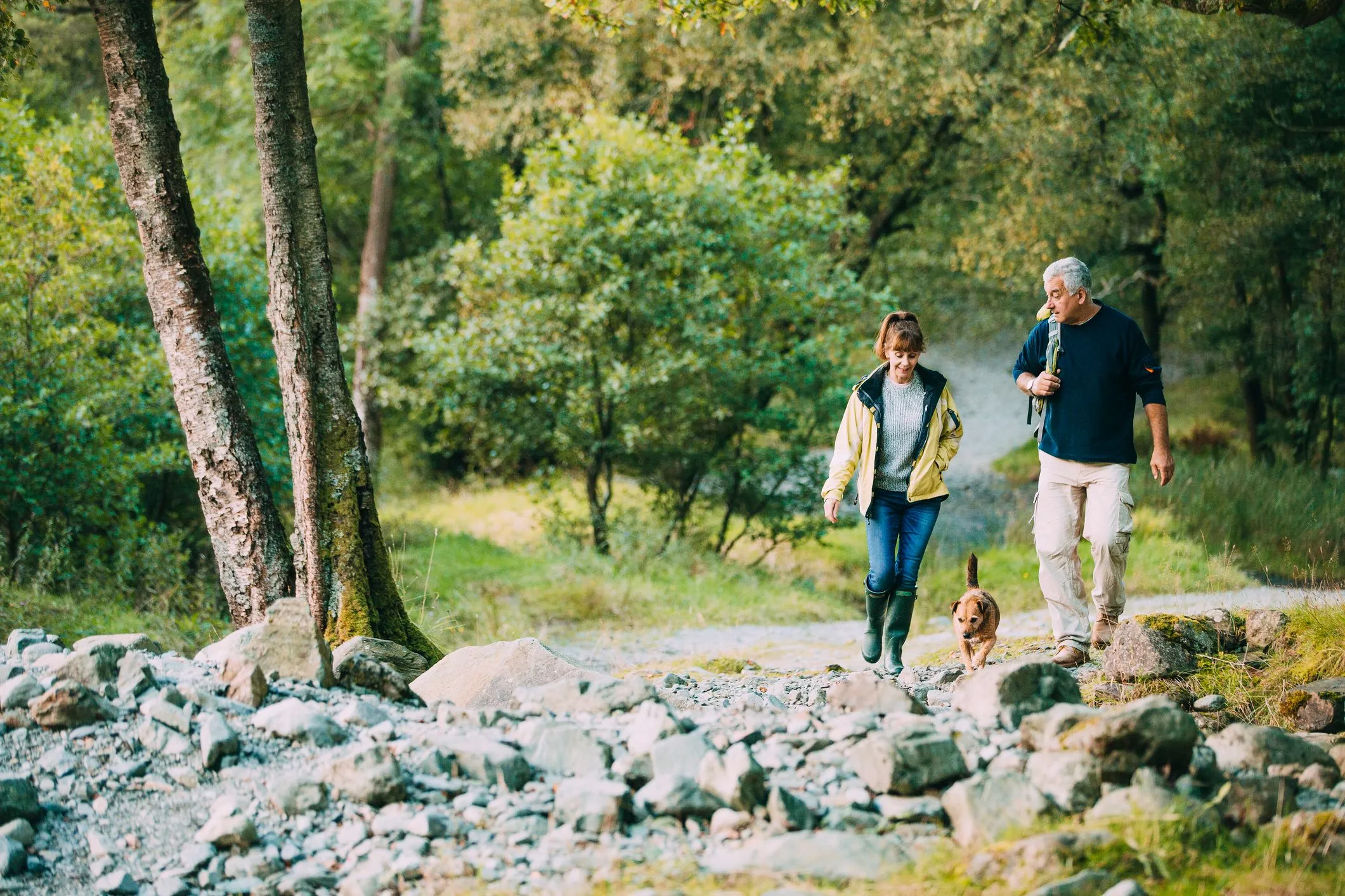 Couple walking a dog along a rocky forest trail