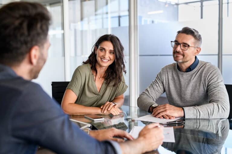 A man and woman engage in conversation with another couple at a conference table during a meeting.