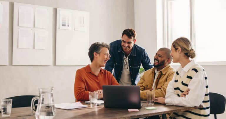 Four people engaged in discussion around a table with a laptop open in front of them.